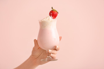 Female hand with glass of tasty milkshake on color background