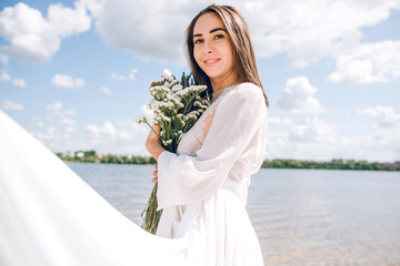 Fototapeta na wymiar beautiful girl in a white dress and holds a bouquet of flowers on the beach
