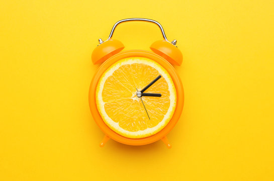 Creative alarm clock with citrus fruit on color background