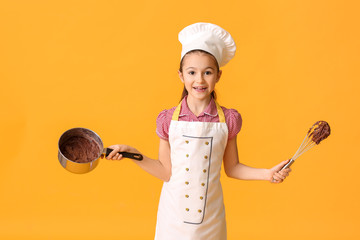Little housewife with melted chocolate in saucepan and whisk on color background
