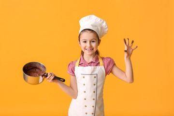 Little housewife with melted chocolate in saucepan on color background