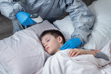 Na pierwszym planie dłoń trzyma termometr elektroniczny gotowy do pomiaru.  W tle twarz chłopca śpiącego w łóżku na białej pościeli.  - obrazy, fototapety, plakaty