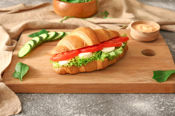 Tasty croissant sandwich on wooden board