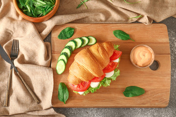 Tasty croissant sandwich with sauce on table