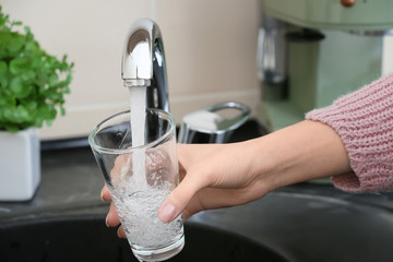 Woman filling glass with fresh water from kitchen faucet