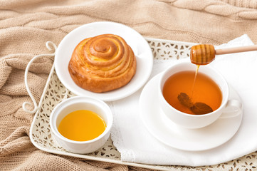 Tasty honey with bun and cup of tea on tray