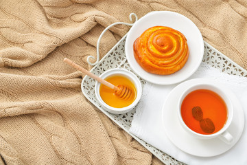 Tasty honey with bun and cup of tea on tray