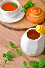 Tasty honey with bun and cup of tea on wooden table