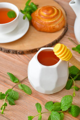 Tasty honey with bun and cup of tea on wooden table
