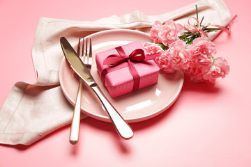 Beautiful table setting with gift and flowers on color background