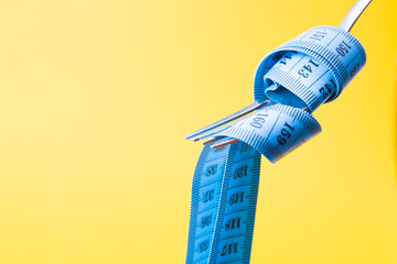 blue measuring tape on a fork like a paste on a yellow background diet concept fasting weight loss...