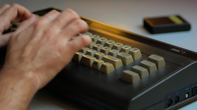 Man hand typing on old 8 bit computer   with a game cartridge from the 80's