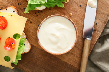 Bowl with tasty cream cheese and sandwiches on table