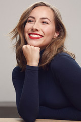 Portrait of a happy young woman sitting at a table with a big smile on her face looking up