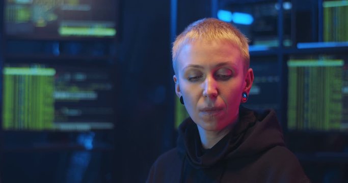 Portrait of Caucasian woman hacker with short hair sitting at night in front of computer. Cyber policewoman turning face to camera and biting cookie. Close up female eating sweets in monitoring room.
