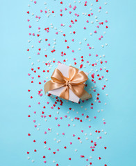 Gift box with golden tied bow, among tiny heart shapes. Top view holiday background.