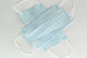 Two simple disposable medical masks made of non-woven fabric lie on a white table