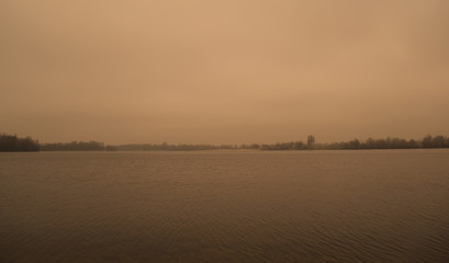 Fototapeta na wymiar A wide landscape of a dark gray lake and forest. Overcast sky