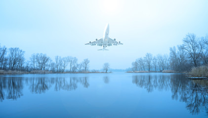 Airplane over the lake and dark trees. The sun is shining