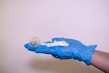 In the hand of the doctor in a blue glove, a used condom with sperm on a white background. Latex...