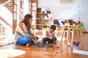 Beautiful teacher and toddler playing with building blocks toy around lots of toys at kindergarten