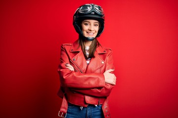 Young beautiful brunette motocyclist woman wearing motorcycle helmet and red jacket happy face smiling with crossed arms looking at the camera. Positive person.