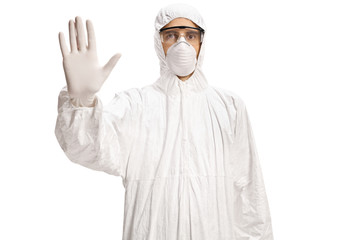 Man in a white hazmat suit and mask gesturing stop with hand