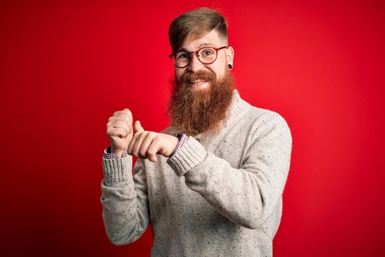 Handsome Irish redhead man with beard wearing casual sweater and glasses over red background Pointing to the back behind with hand and thumbs up, smiling confident
