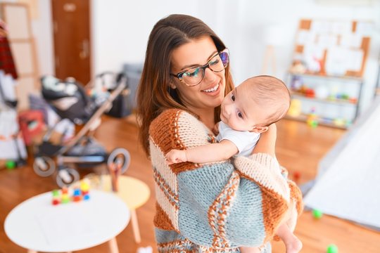 Young beautiful woman and her baby standing at home. Mother holding and hugging newborn
