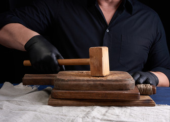 male cook in black uniform holds a wooden hammer for beating meat on a vintage cutting board