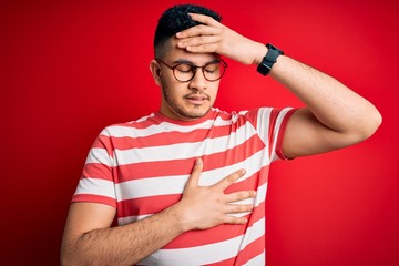 Young handsome man wearing casual striped t-shirt and glasses over isolated red background Touching forehead for illness and fever, flu and cold, virus sick