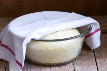 Yeast dough in a glass bowl on a wooden table. Rustic style,.