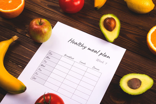 Healthy weekly meal plan among fresh organic fruits and vegetables cooking ingredients on wooden table.