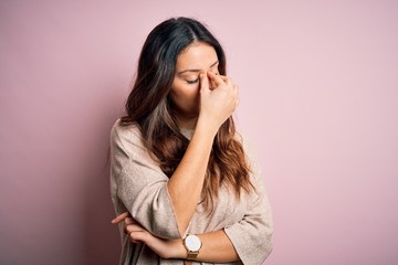 Young beautiful brunette woman wearing casual sweater standing over pink background tired rubbing...