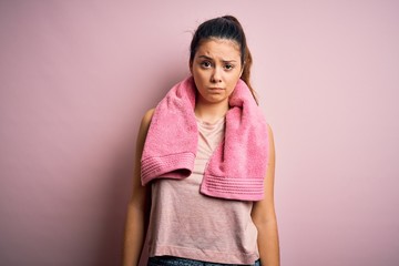 Young beautiful brunette sportswoman wearing sportswear and towel over pink background skeptic and...