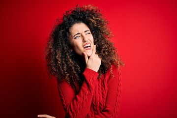 Young beautiful woman with curly hair and piercing wearing casual red sweater Thinking worried about a question, concerned and nervous with hand on chin