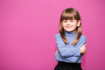 Cute little girl hugs herself, smiling carefree and happy.