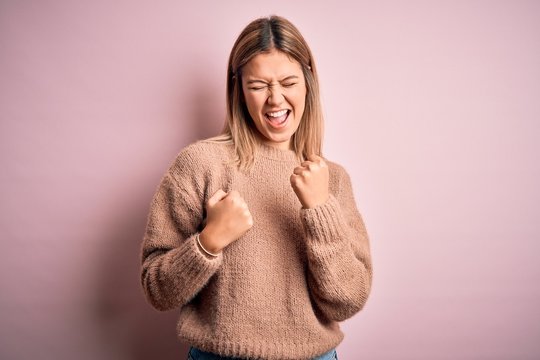 Young beautiful blonde woman wearing winter wool sweater over pink isolated background celebrating surprised and amazed for success with arms raised and eyes closed. Winner concept.