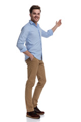 Happy casual man presenting and smiling with hand in pocket