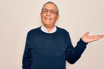 Naklejka premium Senior handsome grey-haired man wearing sweater and glasses over isolated white background smiling cheerful presenting and pointing with palm of hand looking at the camera.