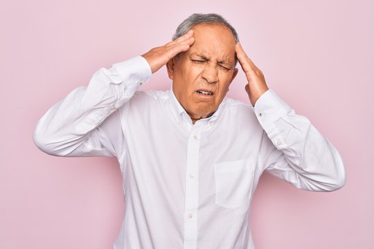 Senior handsome grey-haired man wearing elegant shirt over isolated pink background with hand on head for pain in head because stress. Suffering migraine.
