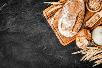 Fresh bakery bread food, rustic crusty loaves of breads and buns on black stone background. Top view and copy space for text.