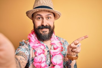 Handsome bald man with beard and tattoo on vacation wearing summer hat and hawaiian lei very happy...