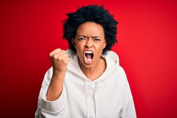 Young beautiful African American afro sportswoman with curly hair wearing sportswear angry and mad raising fist frustrated and furious while shouting with anger. Rage and aggressive concept.