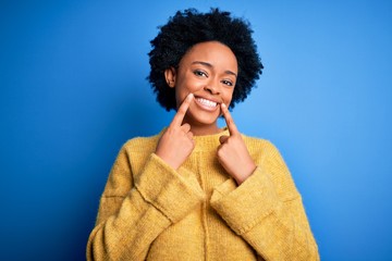 Fototapeta na wymiar Young beautiful African American afro woman with curly hair wearing yellow casual sweater Smiling with open mouth, fingers pointing and forcing cheerful smile
