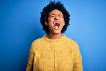 Fototapeta na wymiar Young beautiful African American afro woman with curly hair wearing yellow casual sweater angry and mad screaming frustrated and furious, shouting with anger. Rage and aggressive concept.