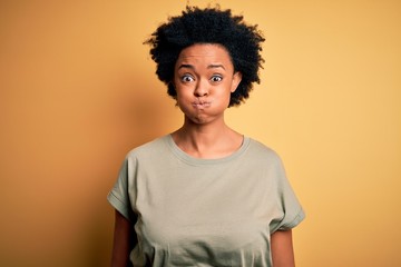 Obraz na płótnie Canvas Young beautiful African American afro woman with curly hair wearing casual t-shirt puffing cheeks with funny face. Mouth inflated with air, crazy expression.