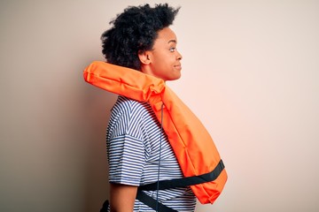 Young African American afro woman with curly hair wearing orange protection lifejacket looking to...