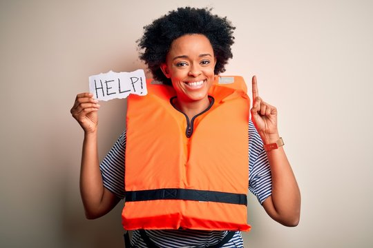 Young African American afro woman with curly hair wearing lifejacket holding help paper surprised with an idea or question pointing finger with happy face, number one