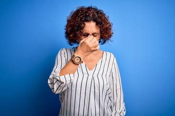 Fototapeta na wymiar Middle age beautiful curly hair woman wearing casual striped shirt over isolated background tired rubbing nose and eyes feeling fatigue and headache. Stress and frustration concept.